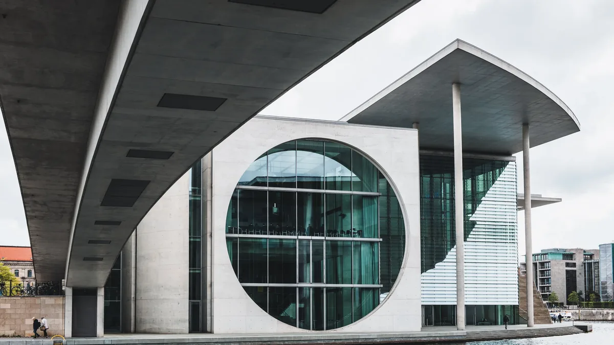 A modern building with a large circular window, a flat roof, and a long overhang, situated in an urban setting.