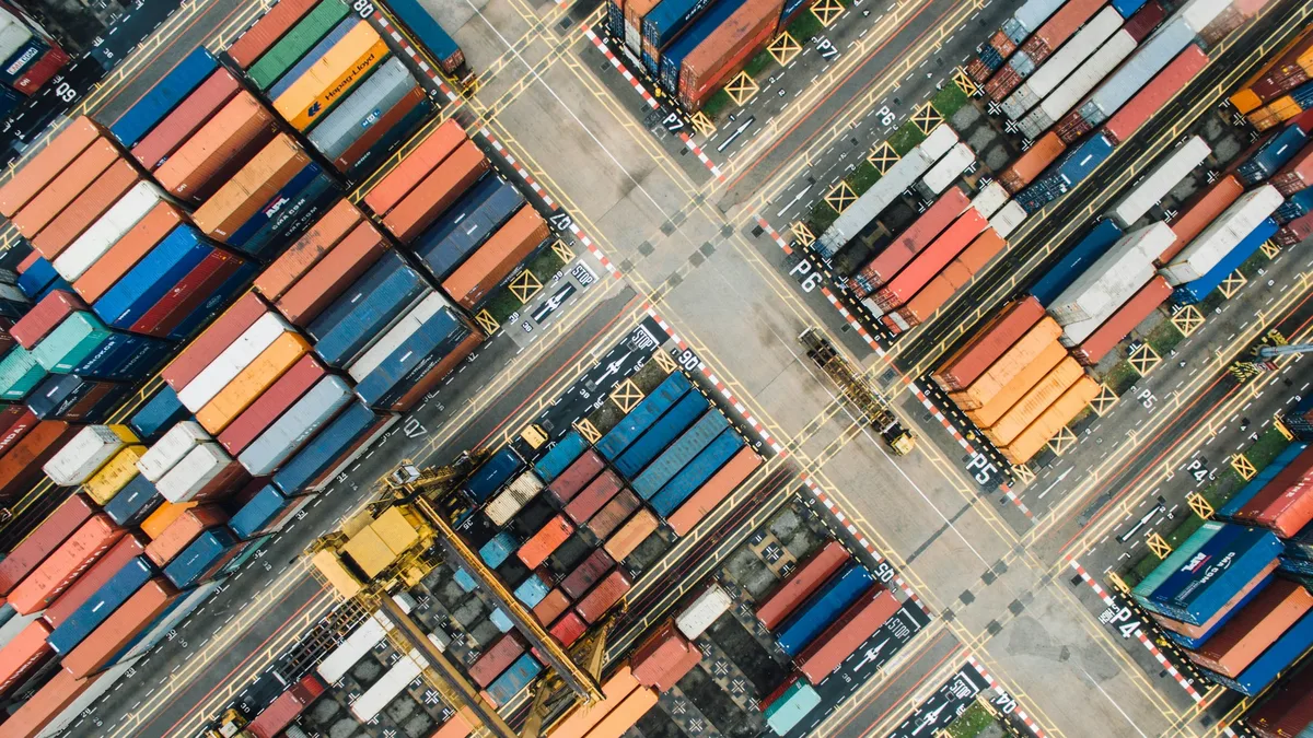 A large number of shipping containers stacked in rows, with some containers being transported by trucks or trains.